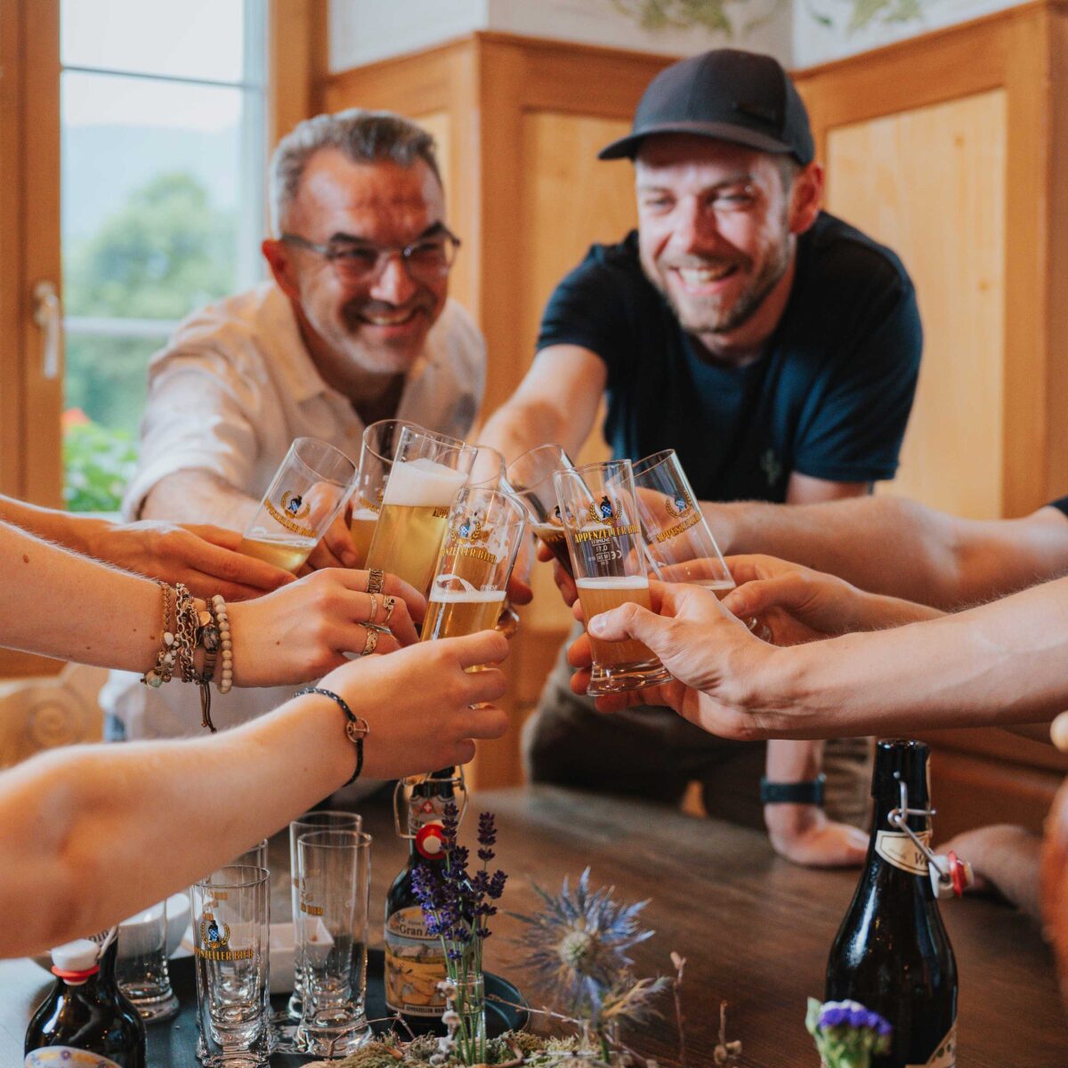 Gruppe stösst mit Appenzeller Biergläsern an einem Holztisch an